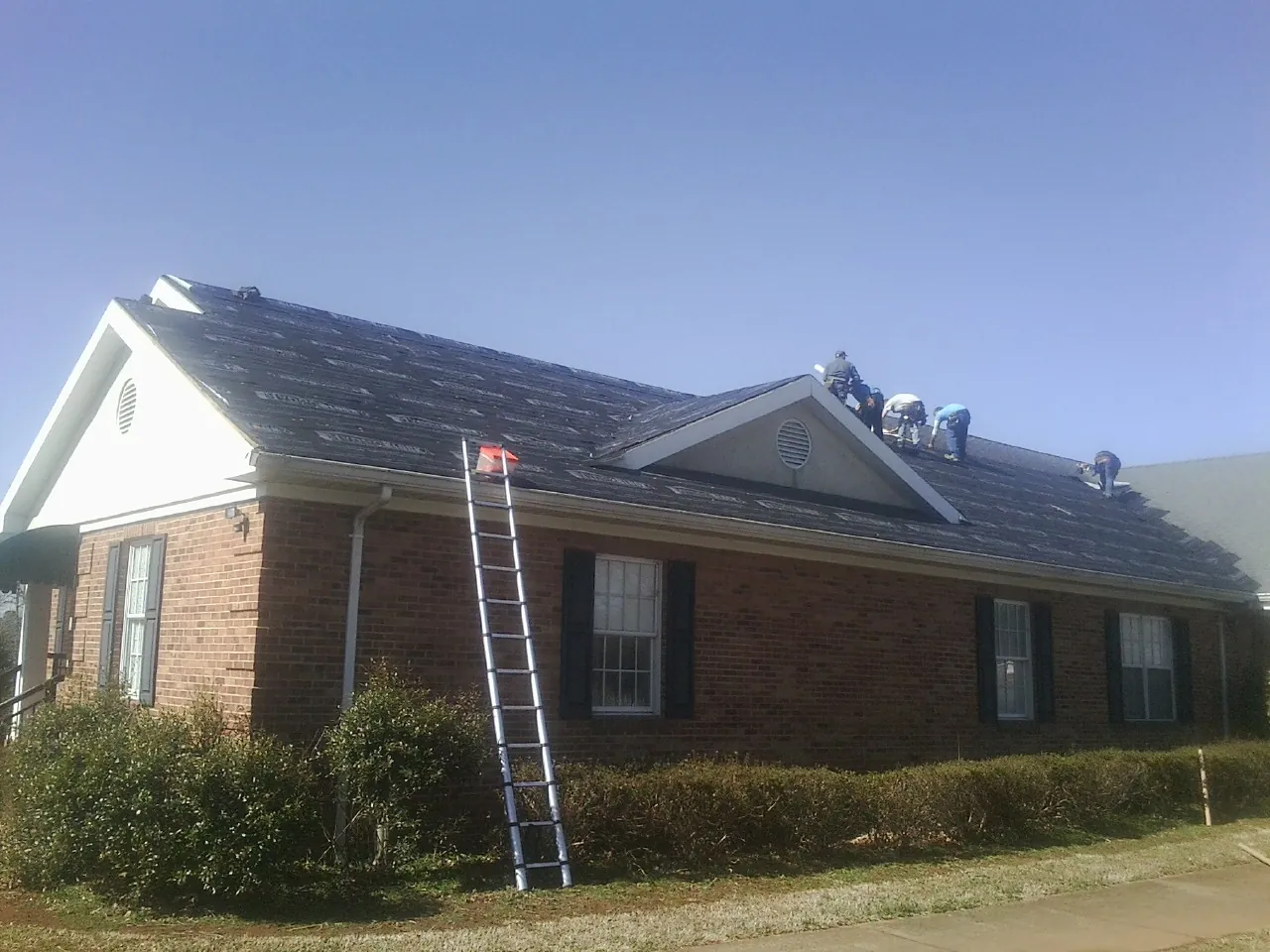 Crew tearing shingles off a brick ranch roof with a ladder set — Metal Roof Repair work by our crew in Fort Monmouth
