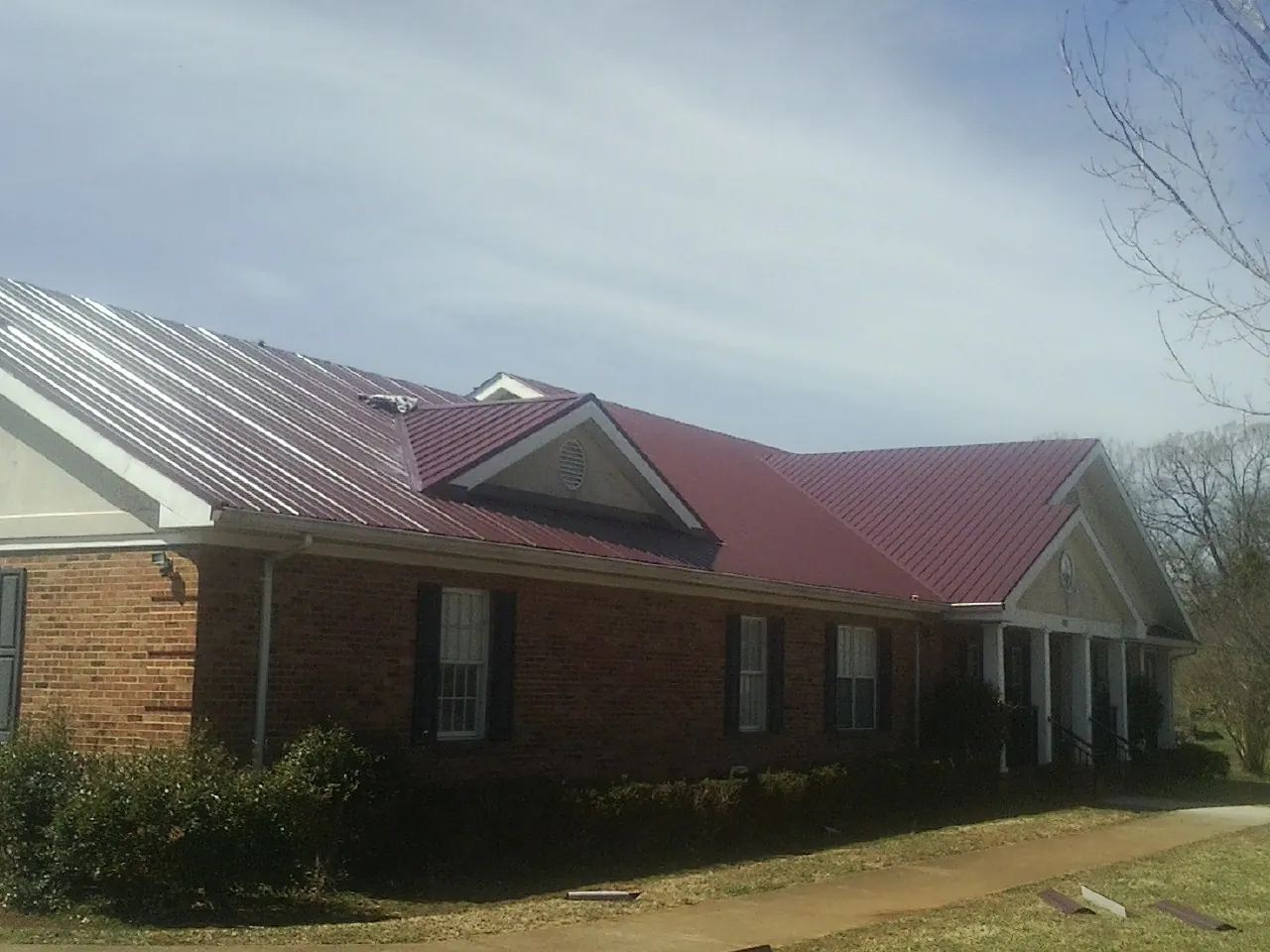 Red metal roof with gabled entries on a long brick building, from a Hail Damage Roof Repair job in Fort Monmouth