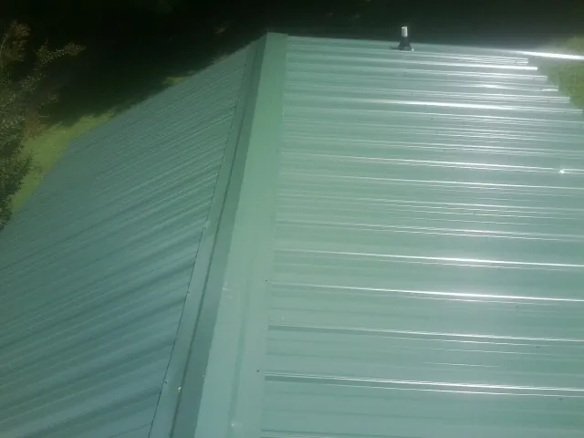 New green metal panels meeting at the ridge of a roof — Flat Roof Repair work by our crew in Fort Monmouth