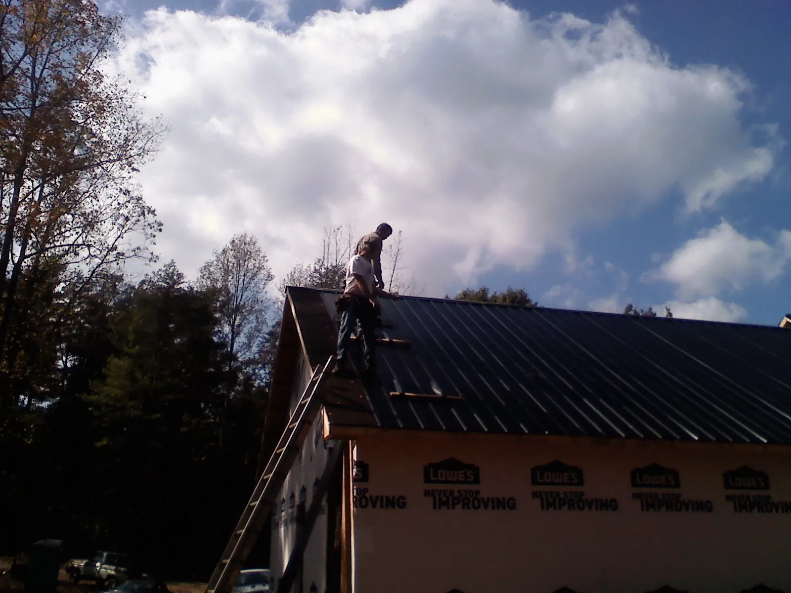 Roofer fastening dark metal panels high against a cloudy sky, from a Roof Inspection job in Fort Monmouth