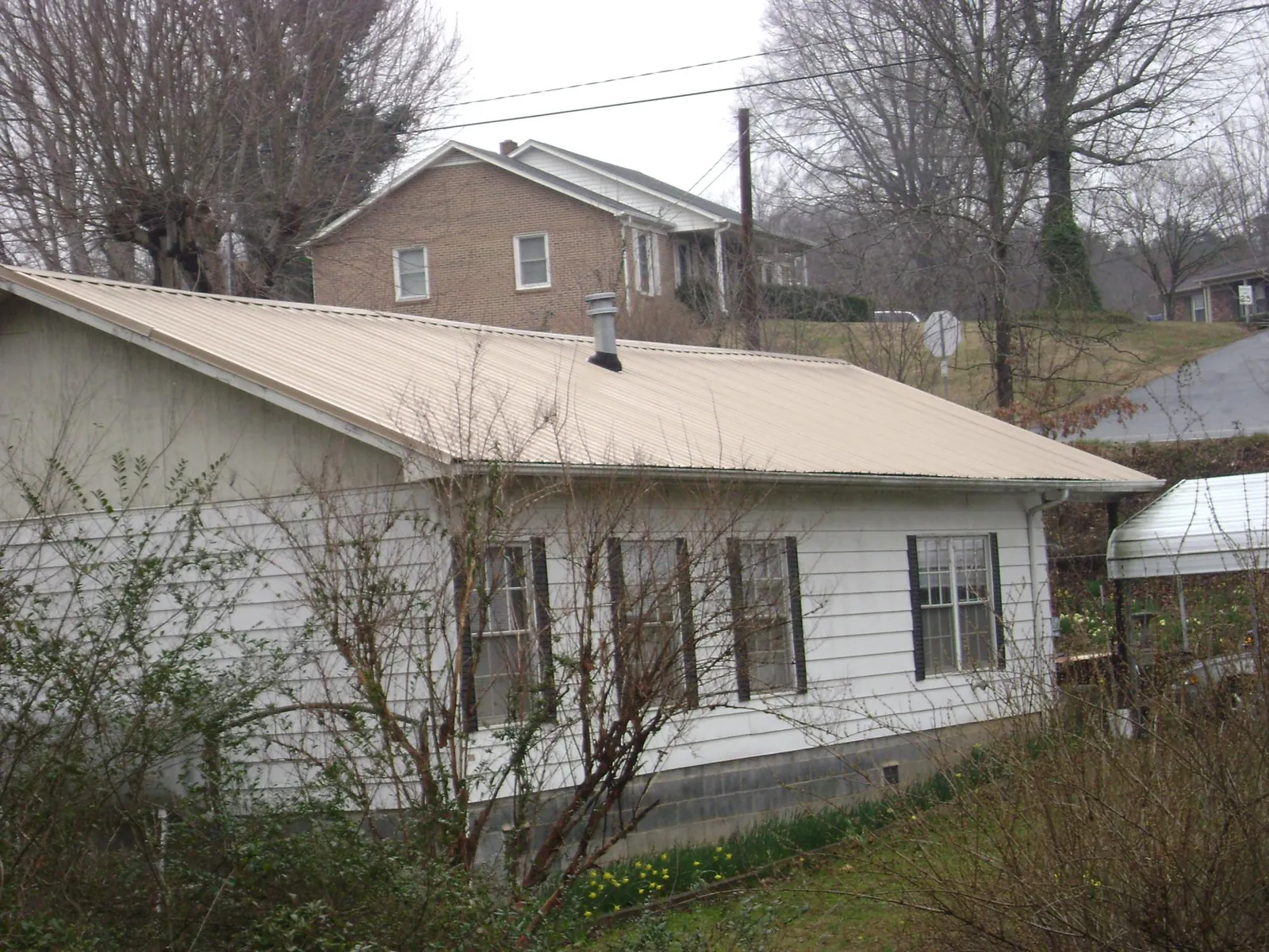 Tan metal roof on a white sided house set into a hillside — Commercial Roofing by Roofing Brothers in Fort Monmouth
